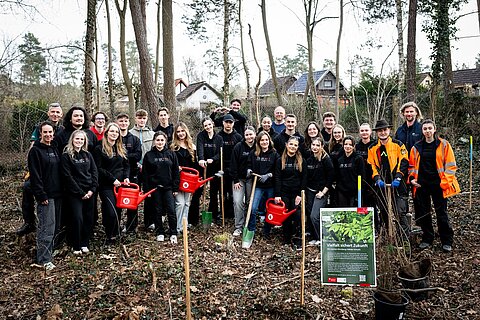 23 Auszubildende der Sparkasse Nürnberg auf einem Gruppenbild gemeinsam mit Forstexperten des Tiergartens und des AELF Fürth-Uffenheim vor der Pflanzung der Bäume in einem Waldstück im Süden Nürnbergs.