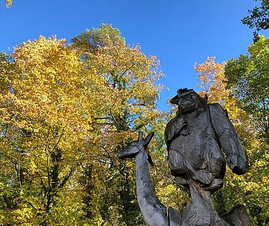 Die Holzstatue im Eingangsbereich des Tiergartens vor buntem Herbstlaub.